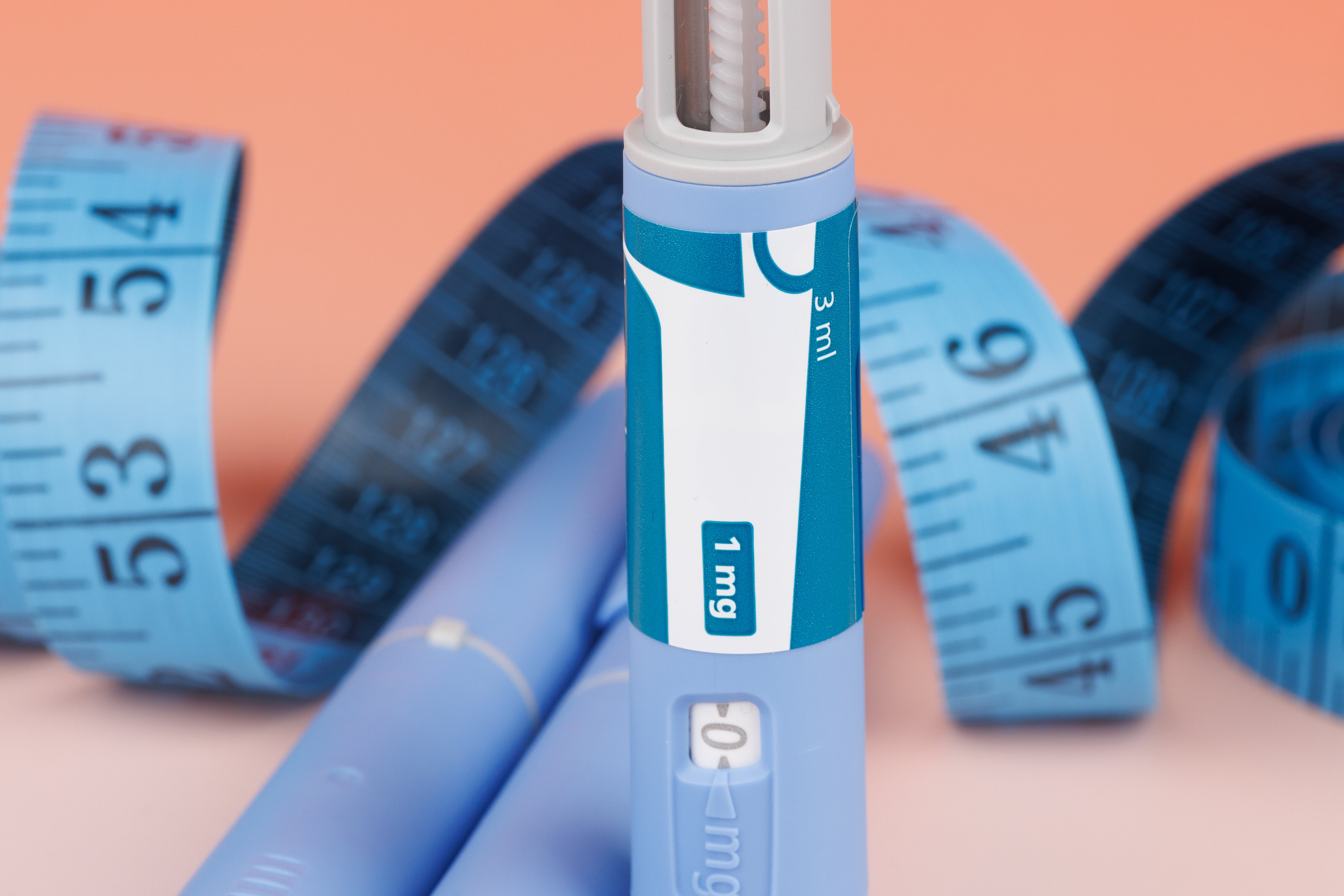 Insulin injection pen with a tape measurer in the background on a pink background