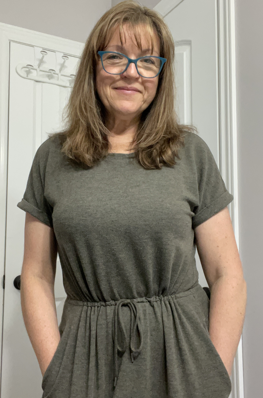 A Livy Method member after shot, who has lost 42 pounds, wearing a green dress standing in a room with a white door