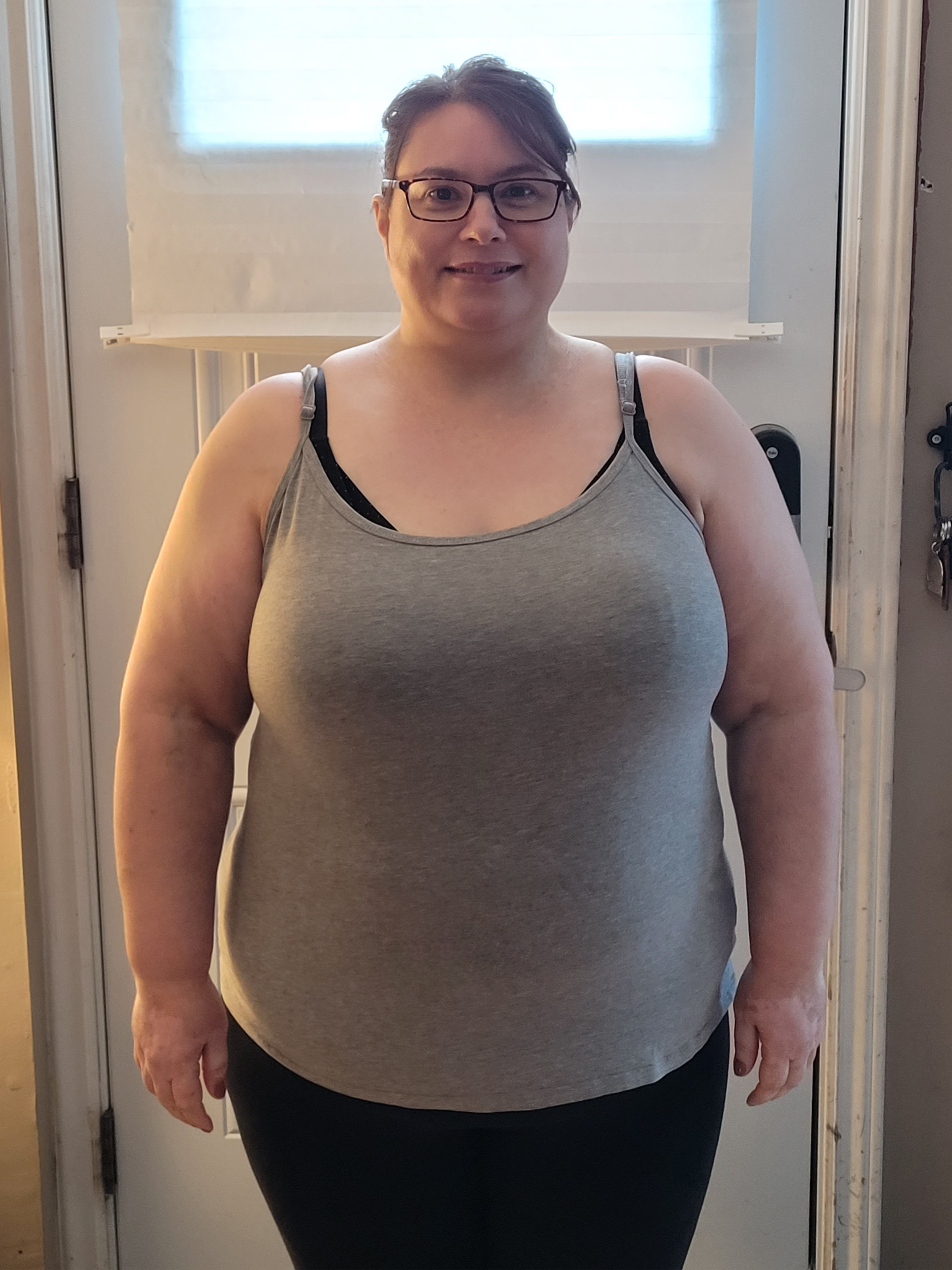 Woman wearing a gray tank top standing in a room with a window in the background
