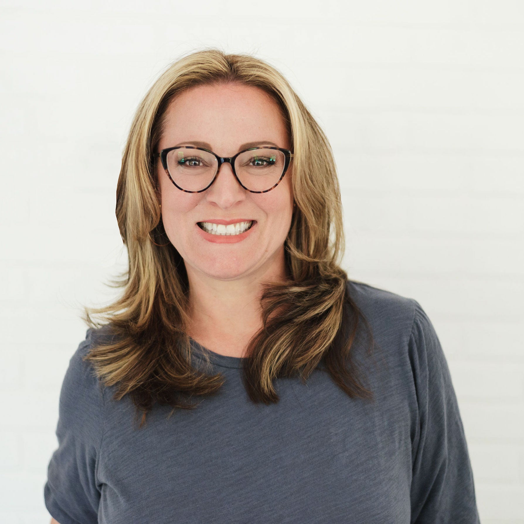 Photo of Dr. Alanna Mcginn wearing a blue long sleeve shirt and glasses, smiling to lens