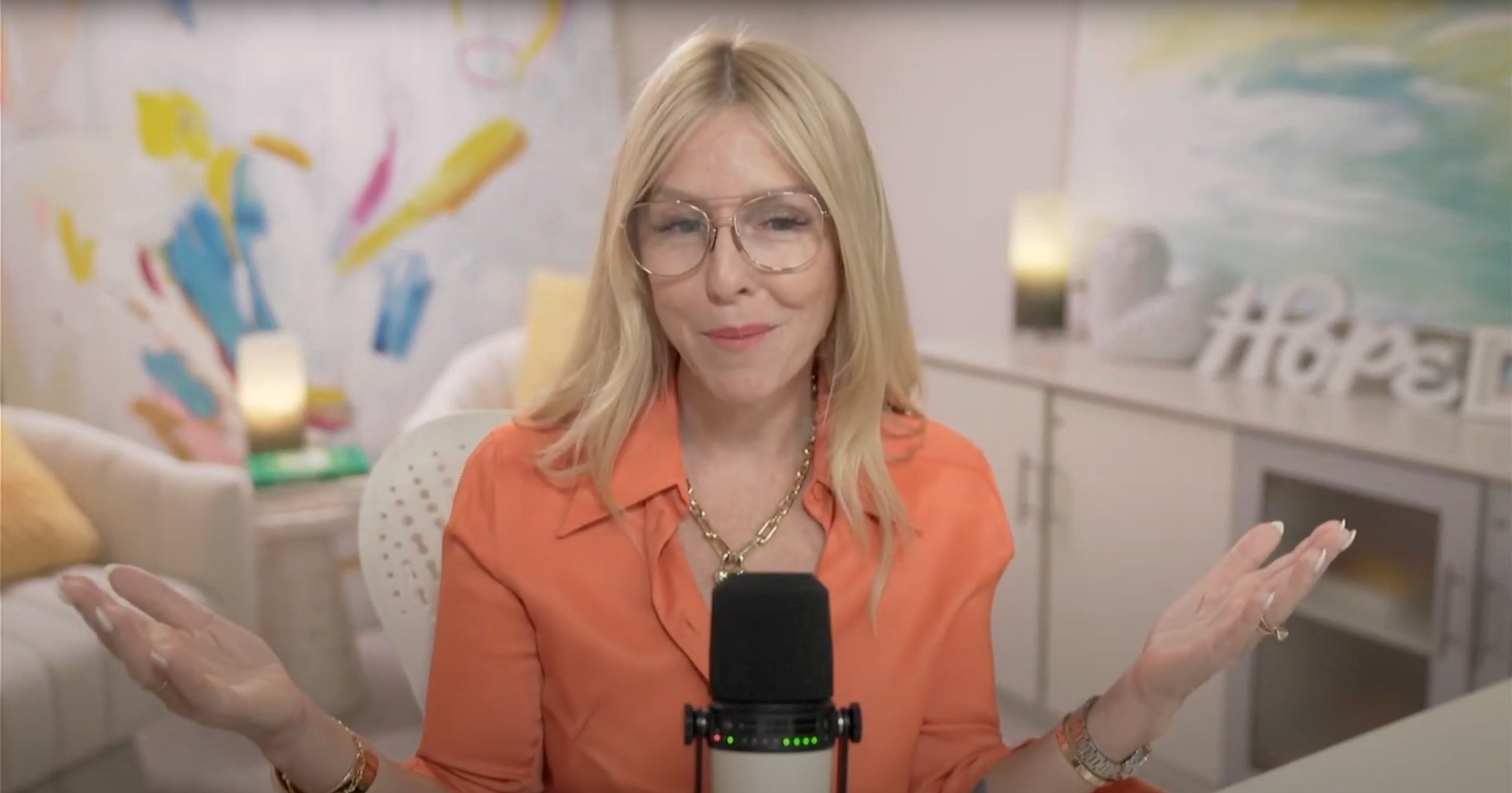 Gina addresses her viewers from her home studio wearing an orange button down